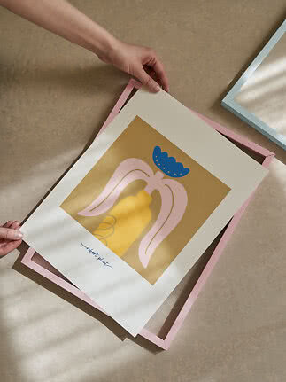 Manos sostienen una lámina de arte abstracto sobre un marco rosa