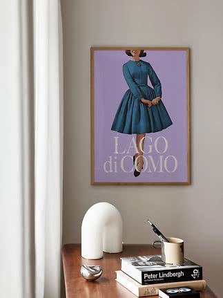 Framed Lago di Como poster with woman in blue dress on purple background above a wooden table