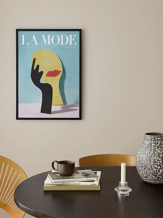 Framed fashion poster with abstract face and black hand on beige wall above round table