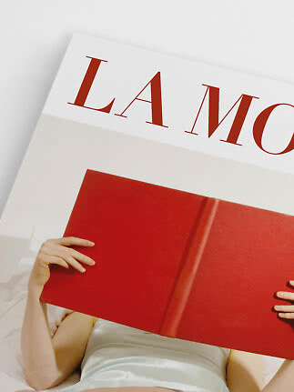Person holding a large red book in front of a magazine cover with red lettering on white background