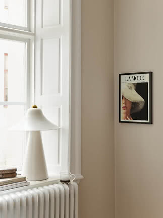 White table lamp on windowsill by radiator, with books, cup and framed poster on beige wall