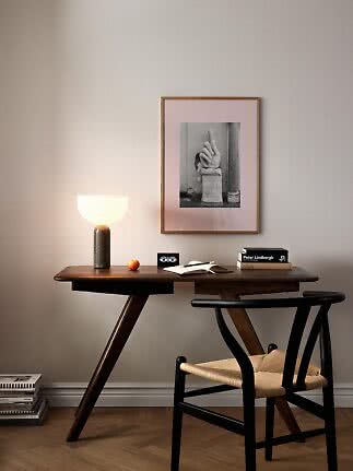 Scrivania in legno scuro con lampada accesa, libri, taccuino aperto e sedia nera sotto quadro incorniciato