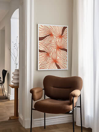 Inramad abstrakt blomsterposter med orange linjer ovanför en brun fåtölj i ett ljust hörn