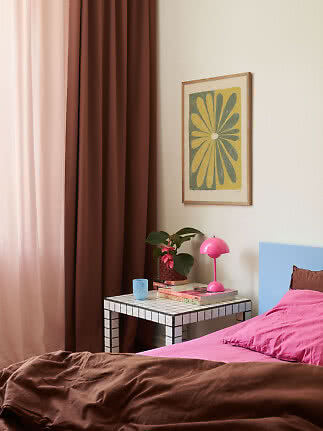 Chambre avec rideaux bruns, lit rose, table carrelée, lampe rose et affiche florale