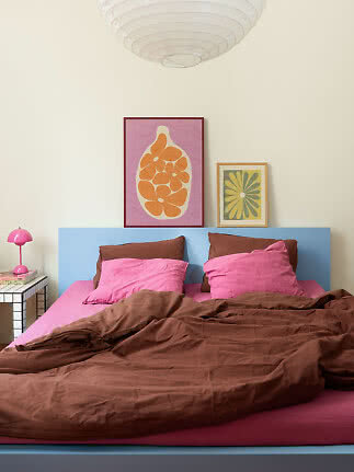 Farbenfrohes Schlafzimmer mit hellblauem Bett, pinker Bettwäsche, brauner Decke und Wandbildern