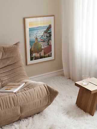 Framed coastal print with domed roof and sea, styled in a bright corner by a lounge chair