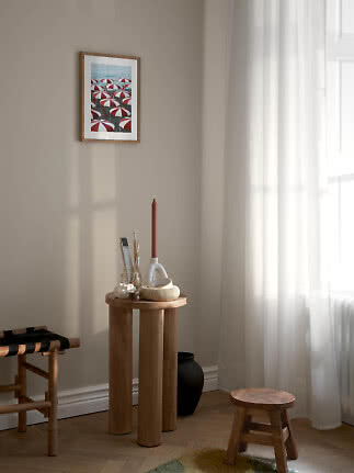 Calm interior corner with wooden stools, round side table and framed print of red-and-white umbrellas.