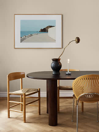 Framed coastal print above a round dining table with vase, branch and lit candle