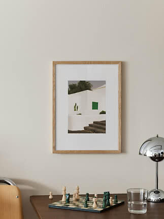 Framed photo print of a white building with green shutters and stone steps on a beige wall