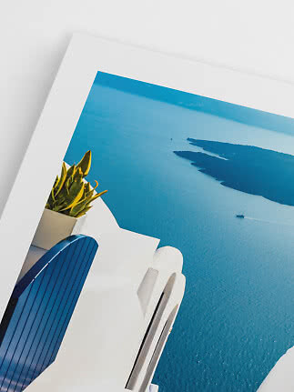 White balcony with blue chair and plant overlooking bright blue sea and coastline