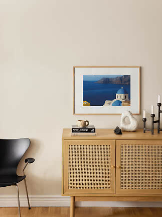 Light wood cabinet with cane doors, black chair, and framed sea photo on a beige wall.