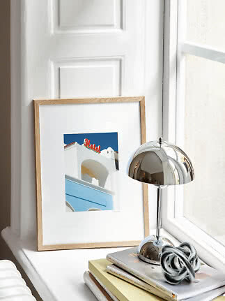 Framed print by a window with chrome lamp, books and decorative knot on a white sill