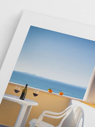 Angled view of terrace with white table, chair, wine bottle, two glasses of red wine, and sea view