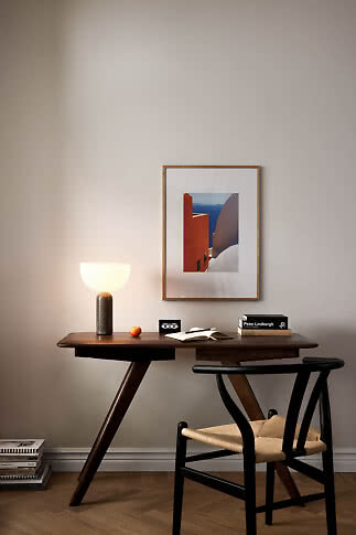 Dark wooden desk with glowing table lamp, books, notebook and black chair beneath framed wall art.