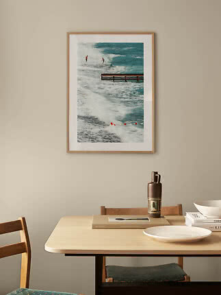 Framed ocean photo with surfers and waves hanging above a dining table