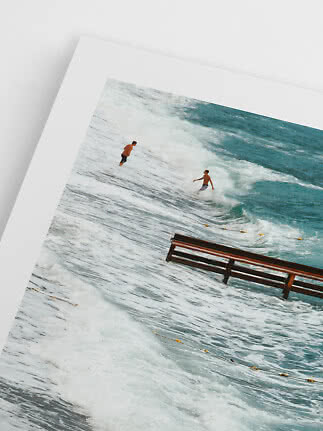 Framed beach photo with two surfers in the waves and a partially submerged bench
