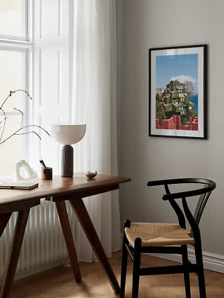 Framed art print above a desk and black chair in a bright, modern room