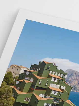Printed photo of a green building with terracotta roofs by the coast and mountains under blue sky