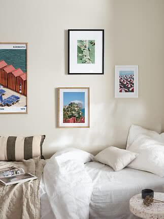 Bright bedroom with white bed, pillows, striped cushion and four framed wall prints