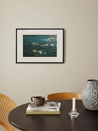 Photo encadrée de nageurs en mer sur mur beige au-dessus d'une table sombre