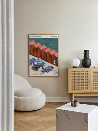 Framed vintage travel poster with beach huts and blue loungers on a beige wall