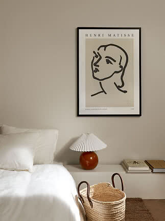 Soveværelse med Matisse-plakat over hvid seng, orange lampe og flettet kurv
