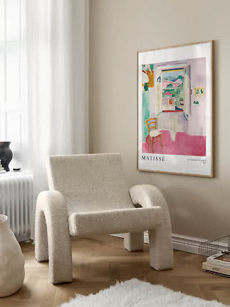 Indrammet Matisse-plakat på beige væg over en cremefarvet loungestol ved et vindue