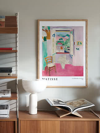 Indrammet Matisse-plakat på væg over træskab med hvid lampe og åben bog