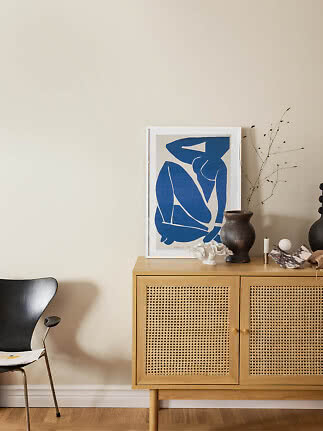 Lyst træskab med flettede låger, blå kunstplakat, mørk vase og dekor på beige væg