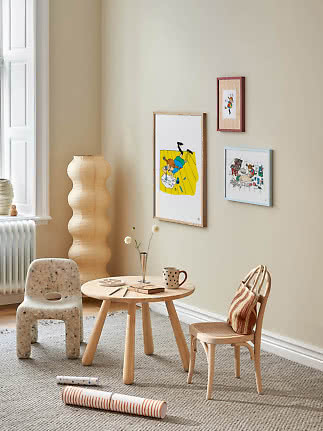 Cozy children's room with a small wooden table, two chairs, floor lamp, and three framed posters on the wall.