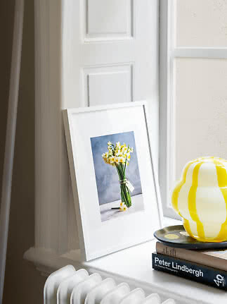 Cadre blanc avec photo de fleurs sur rebord de fenêtre, près d'une lampe jaune rayée