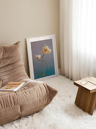 Affiche florale encadrée posée contre le mur près d'un fauteuil beige, tapis blanc et table en bois