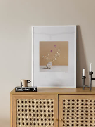 White framed floral print with vase on beige wall above a light wood cabinet
