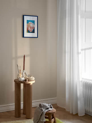 Blau gerahmter Blumendruck an beiger Wand über rundem Holztisch neben hellem Fenster