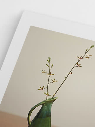 Green ceramic vase with delicate flowering branches against a light wall