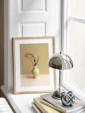 Indrammet blomsterprint på vindueskarm ved siden af kromlampe og stak bøger