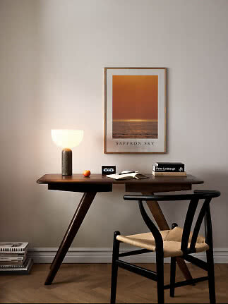 Mørkt træskrivebord med sort stol, tændt bordlampe og orange plakat på væggen