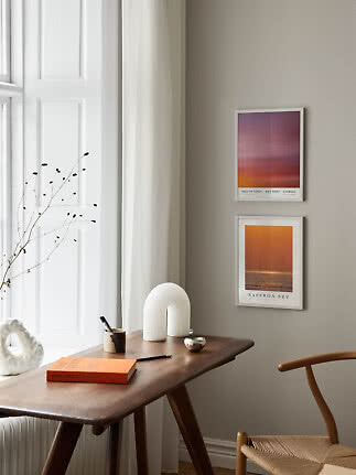 Coin cosy avec bureau en bois, chaise, vase et deux affiches encadrées sur mur beige
