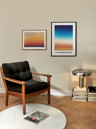 Coin salon avec fauteuil noir en bois, deux affiches colorées et lampe chromée sur des livres
