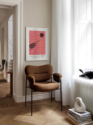 Brauner Polsterstuhl mit schwarzen Beinen in heller Ecke neben Fenster und Wandbild