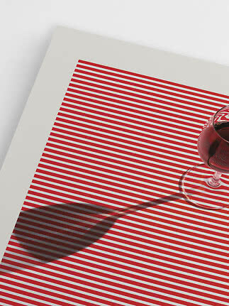 Weinglas mit Rotwein auf weißer Fläche mit roten Streifen und deutlichem Schatten