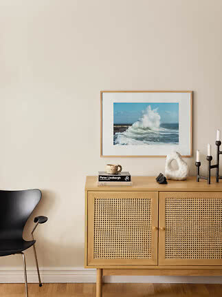 Aparador de madera clara con puertas de rejilla, cuadro del mar, candelabros y silla negra