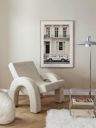 Framed photo of a white vintage car outside a classic building above a plush lounge chair