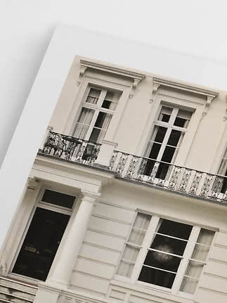Tilted view of a white classic building with black balcony railings, tall windows and columns