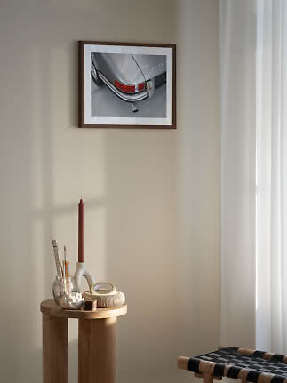 Indrammet foto af bagenden på en sølvgrå klassisk bil på en beige væg