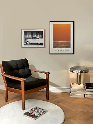 Modern dark fabric and wood armchair beside lamp, books and wall art in a stylish room corner