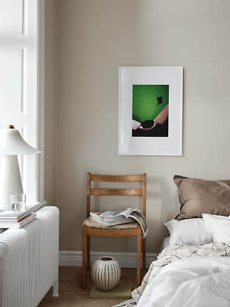 Hyggeligt soveværelseshjørne med træstol, seng, lampe og indrammet billede på beige væg