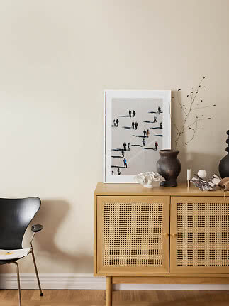 Light wood sideboard with cane doors, vase and framed art against a beige wall