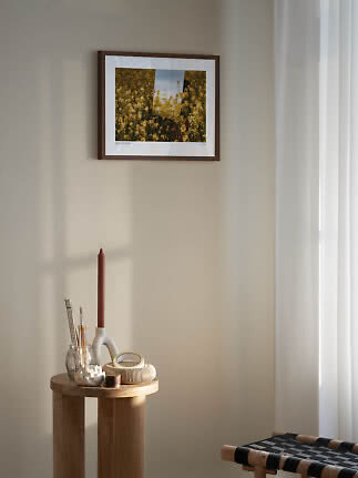 Indrammet kunsttryk med gule blomster på beige væg over et lille træbord med lys og dekorationer