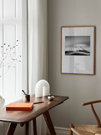 Indrammet sort-hvid bjergfoto på væg over træskrivebord i lyst, minimalistisk rum